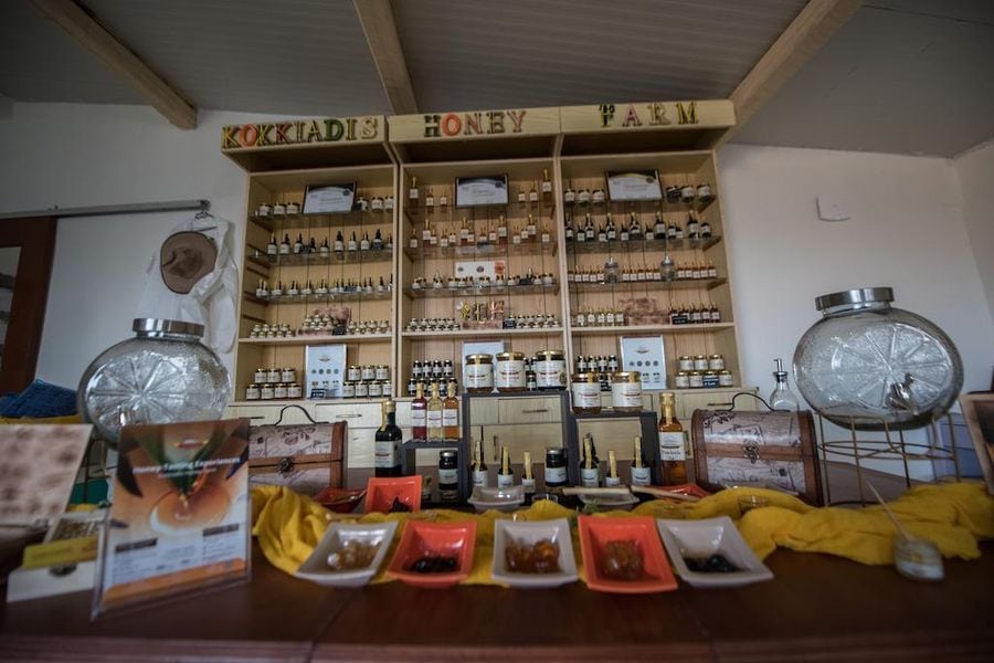 close-up of a table with plates with honey and a cupboard with shelves of bee products in the background at Kokkiadis honey farm